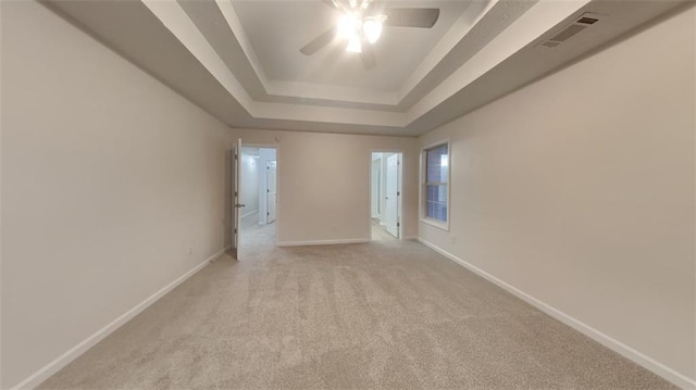 unfurnished room with visible vents, baseboards, light colored carpet, a tray ceiling, and a ceiling fan