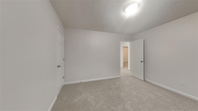 spare room with light colored carpet, a textured ceiling, and baseboards