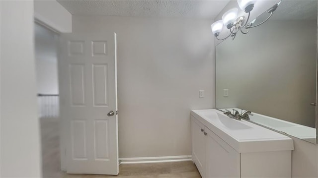 bathroom with baseboards, a chandelier, vanity, wood finished floors, and a textured ceiling