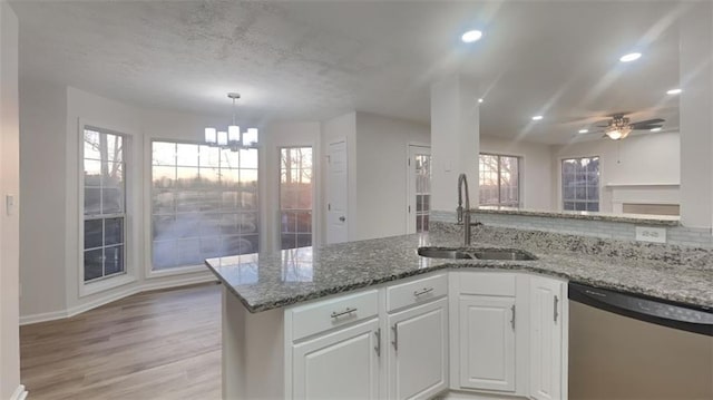 kitchen with light wood finished floors, white cabinetry, stone countertops, a sink, and dishwasher