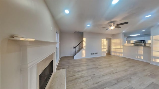 unfurnished living room featuring light wood-type flooring, visible vents, recessed lighting, stairway, and a fireplace