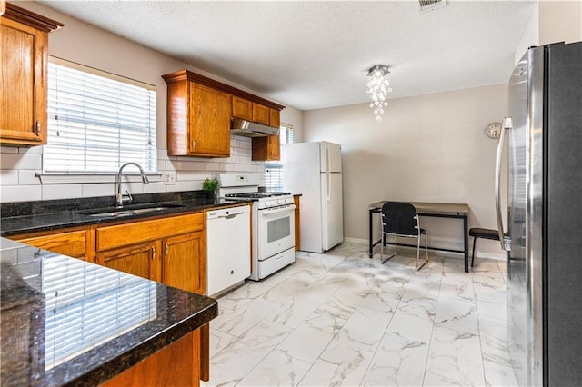 kitchen featuring a textured ceiling, white appliances, backsplash, and sink