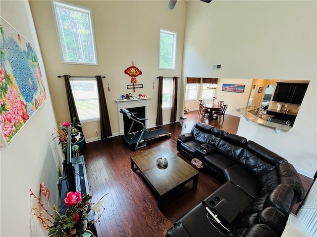 living area with a wealth of natural light, dark wood-style flooring, baseboards, and a high ceiling