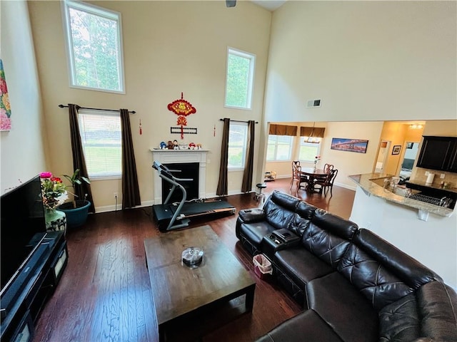 living area with a fireplace with raised hearth, dark wood finished floors, visible vents, and a healthy amount of sunlight