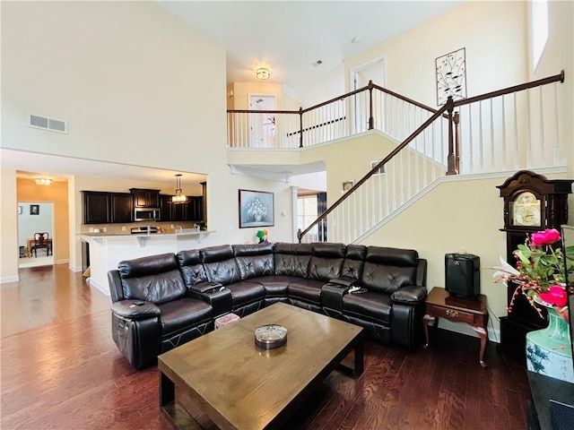 living area featuring a high ceiling, stairs, visible vents, and dark wood-type flooring