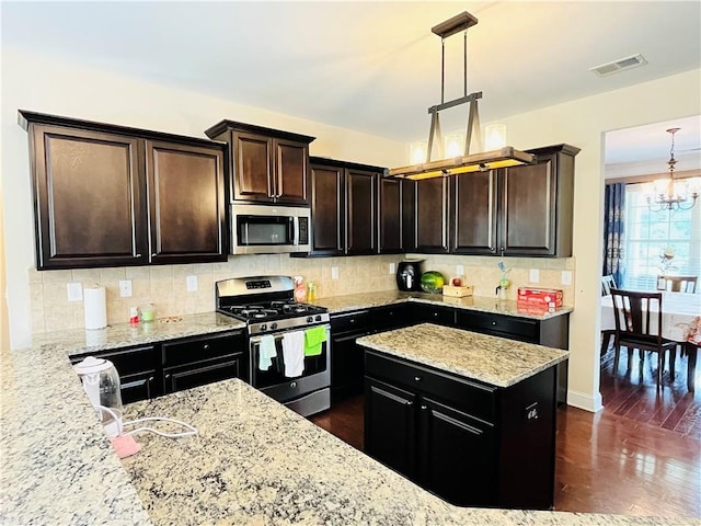 kitchen featuring light stone counters, stainless steel appliances, tasteful backsplash, visible vents, and an inviting chandelier