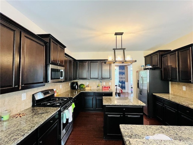 kitchen with a kitchen island, appliances with stainless steel finishes, light stone counters, dark wood-type flooring, and backsplash