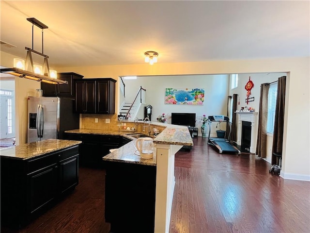 kitchen with a fireplace with raised hearth, a sink, open floor plan, dark cabinetry, and stainless steel fridge