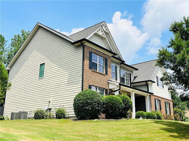 view of side of property with a yard, brick siding, and roof with shingles