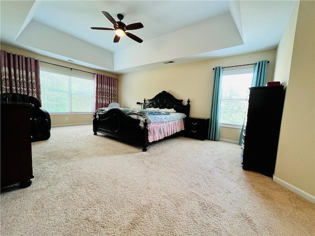 carpeted bedroom featuring visible vents, a raised ceiling, a ceiling fan, and baseboards