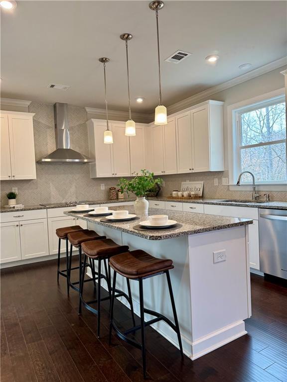 7580 Sunridge Ln, Douglasville, GA 30135 - kitchen featuring ornamental molding, stainless steel dishwasher, a kitchen island, visible vents, and wall chimney range hood