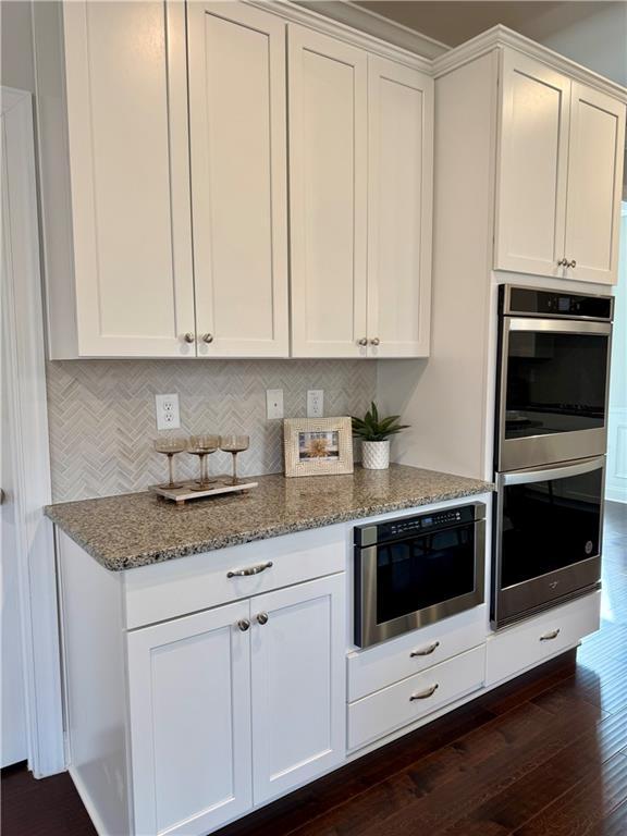 7580 Sunridge Ln, Douglasville, GA 30135 - kitchen with dark wood-style floors, double oven, light stone countertops, and white cabinets