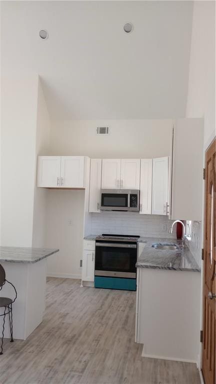 kitchen with stainless steel appliances, backsplash, white cabinetry, a sink, and light stone countertops