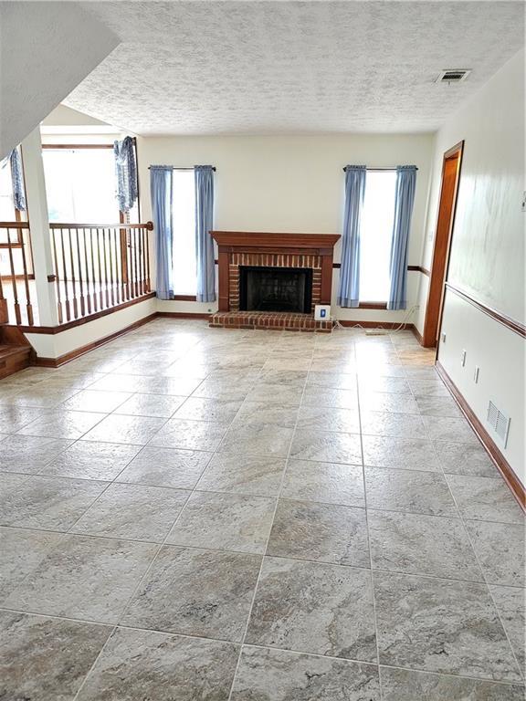2752 Inverloch Cir, Duluth, GA 30096 - unfurnished living room with baseboards, plenty of natural light, a textured ceiling, a fireplace, and stone tile floors