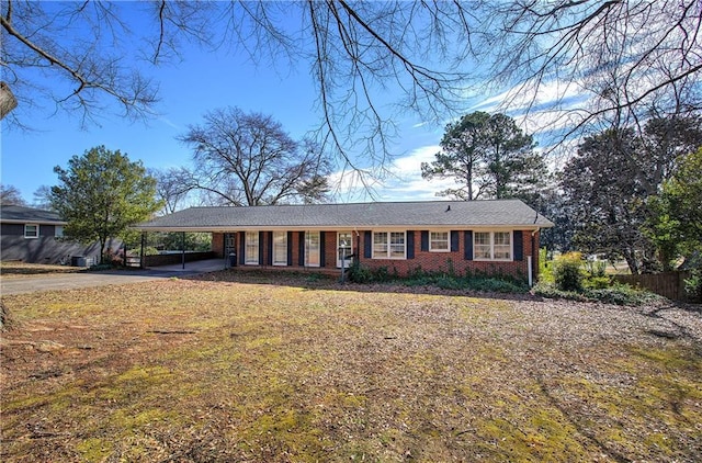 ranch-style home featuring driveway, fence, a front lawn, a carport, and brick siding