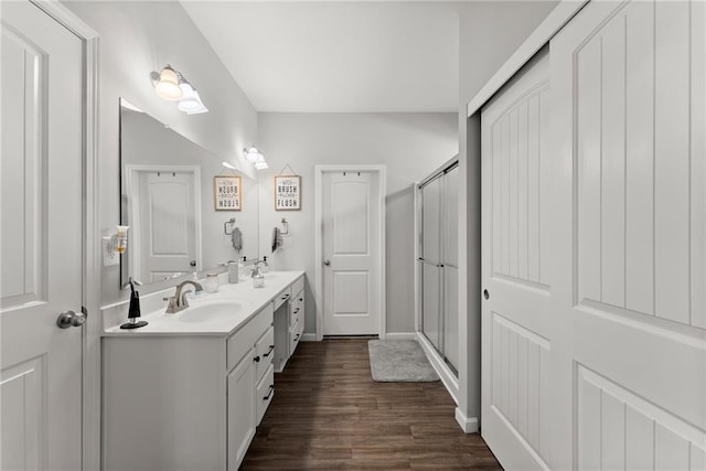 bathroom featuring double vanity, a stall shower, a sink, and wood finished floors