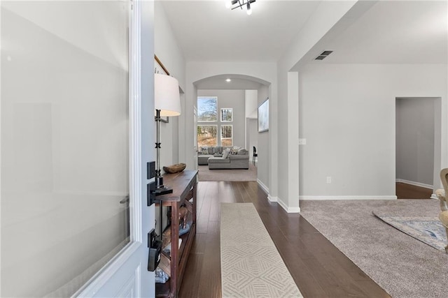 hall featuring dark wood-style floors, arched walkways, visible vents, and baseboards