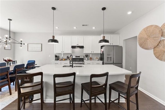 kitchen with an island with sink, appliances with stainless steel finishes, decorative light fixtures, light countertops, and a sink