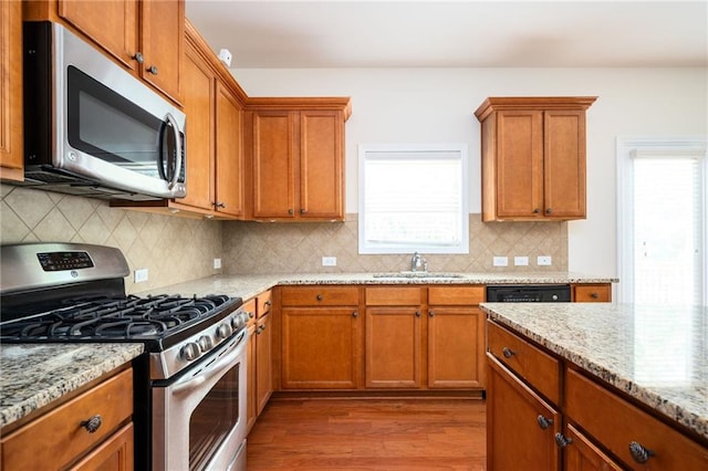 558 Olympic Way, Acworth, GA 30102 - kitchen with stainless steel appliances, wood finished floors, brown cabinetry, light stone counters, and decorative backsplash