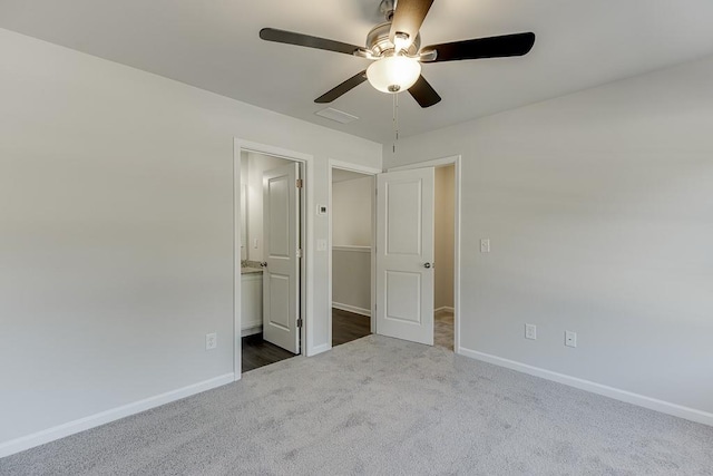 unfurnished bedroom featuring ceiling fan, ensuite bathroom, and dark colored carpet