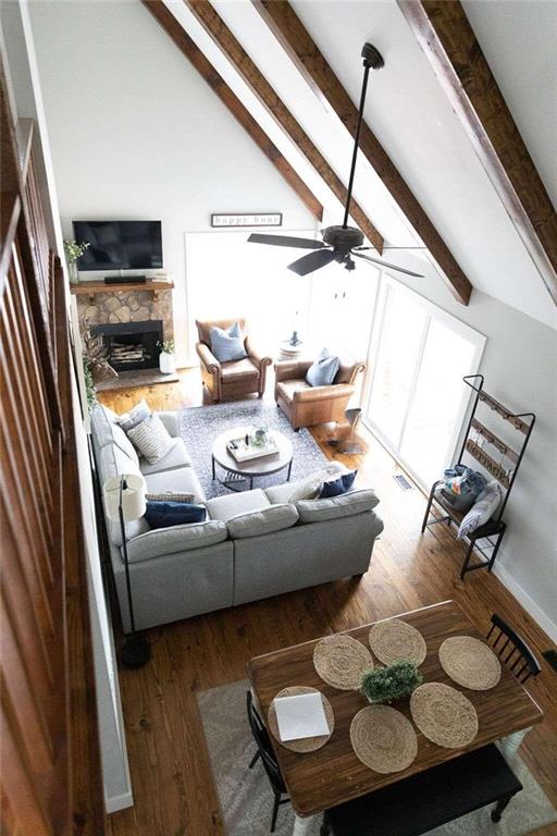 living room with ceiling fan, hardwood / wood-style flooring, high vaulted ceiling, beamed ceiling, and a stone fireplace