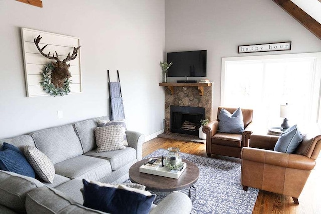living room with beamed ceiling, high vaulted ceiling, a stone fireplace, and hardwood / wood-style flooring
