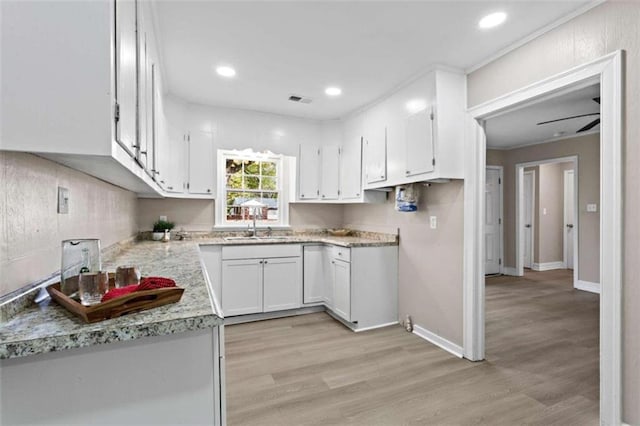 kitchen with sink, white cabinets, ceiling fan, light stone counters, and light wood-type flooring