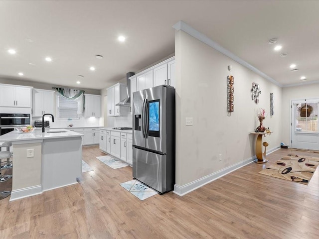 kitchen with light wood-style flooring, stainless steel appliances, a sink, white cabinets, and wall chimney range hood