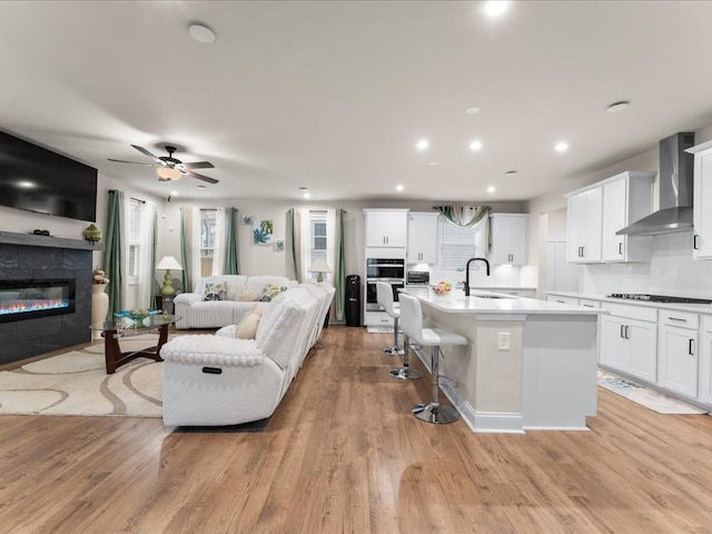 living room featuring a ceiling fan, a glass covered fireplace, light wood finished floors, and recessed lighting