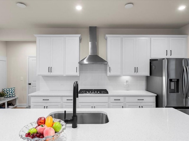 kitchen featuring stainless steel fridge, wall chimney exhaust hood, backsplash, gas stovetop, and a sink