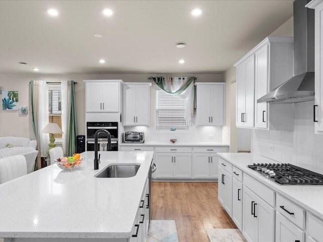 kitchen featuring stainless steel appliances, white cabinets, a sink, light wood-type flooring, and wall chimney exhaust hood