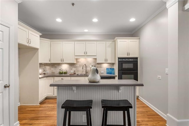 kitchen with light wood finished floors, white cabinets, dobule oven black, and backsplash