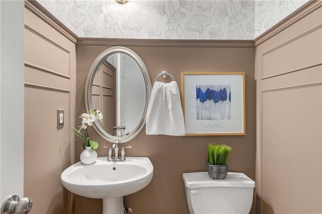 half bath featuring wallpapered walls, toilet, and a sink