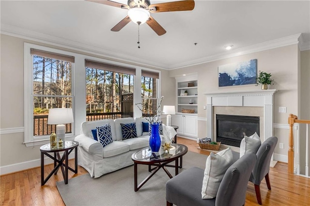 living area with light wood-type flooring, baseboards, a glass covered fireplace, and crown molding