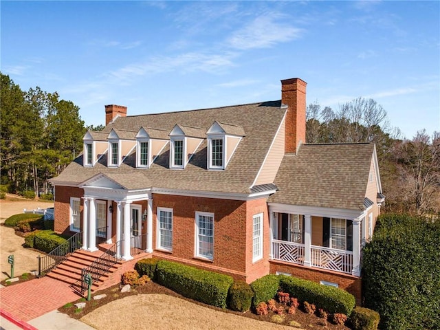 cape cod house with brick siding, a porch, a chimney, and a shingled roof