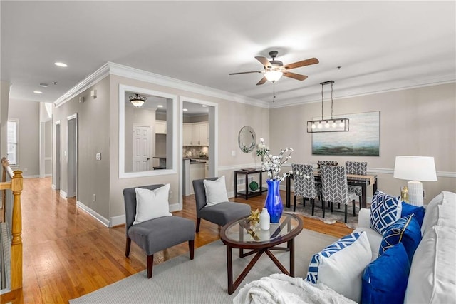 living area featuring a ceiling fan, baseboards, light wood finished floors, recessed lighting, and crown molding
