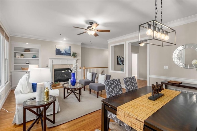 dining space with crown molding, ceiling fan, built in features, light wood-type flooring, and a glass covered fireplace