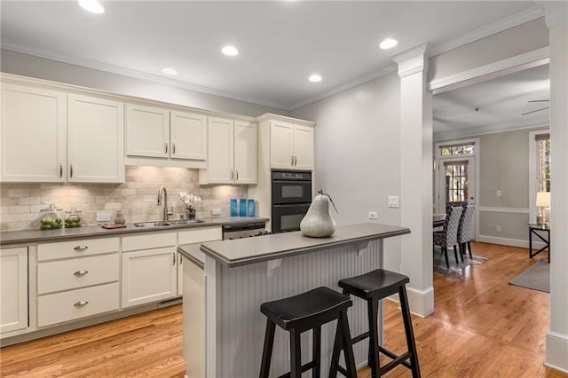 kitchen with dobule oven black, a sink, a kitchen breakfast bar, crown molding, and light wood finished floors