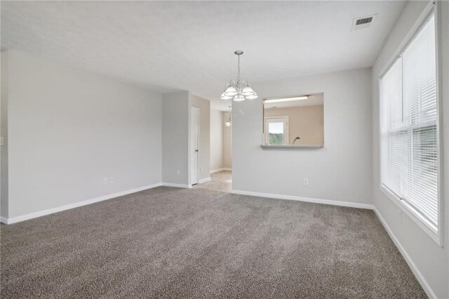 empty room with visible vents, carpet floors, a notable chandelier, and baseboards