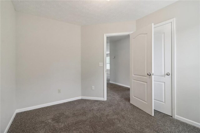 spare room with dark carpet, a textured ceiling, and baseboards