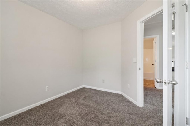 empty room with baseboards, dark carpet, and a textured ceiling