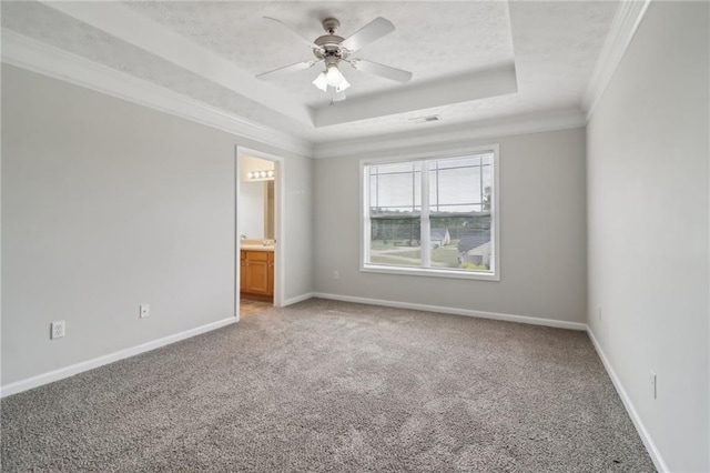 empty room with a tray ceiling, crown molding, baseboards, and light carpet