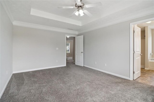 carpeted spare room featuring ornamental molding, baseboards, a tray ceiling, and a ceiling fan