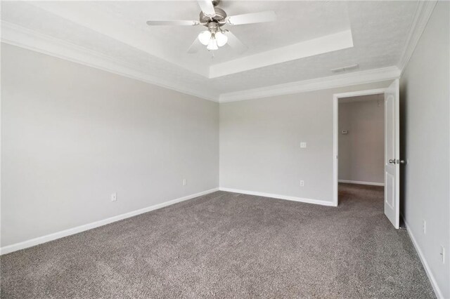 unfurnished room with a raised ceiling, crown molding, dark colored carpet, and baseboards