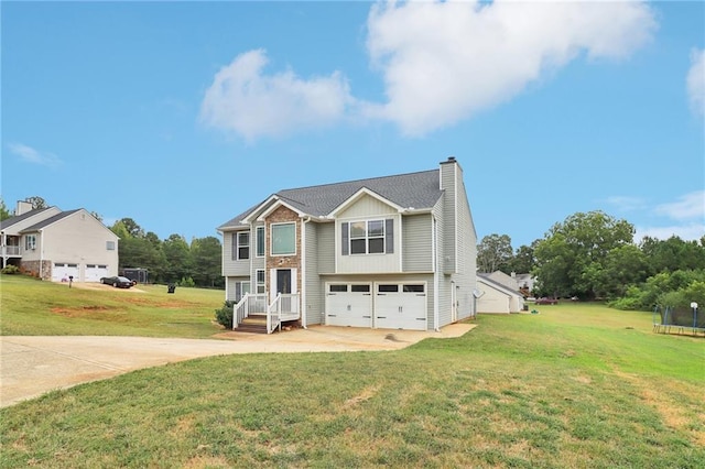 bi-level home with a chimney, concrete driveway, a front lawn, a garage, and a trampoline