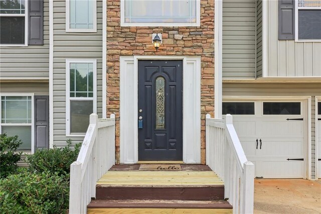 property entrance featuring stone siding, an attached garage, and driveway