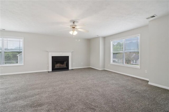 unfurnished living room featuring a fireplace with flush hearth, carpet floors, plenty of natural light, and a ceiling fan