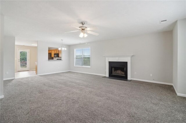 unfurnished living room featuring carpet flooring, plenty of natural light, ceiling fan with notable chandelier, and visible vents
