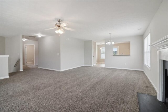 unfurnished living room featuring baseboards, carpet floors, a healthy amount of sunlight, and ceiling fan with notable chandelier