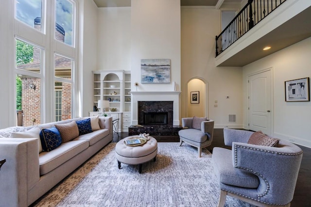 living room with a fireplace, visible vents, a towering ceiling, wood finished floors, and baseboards